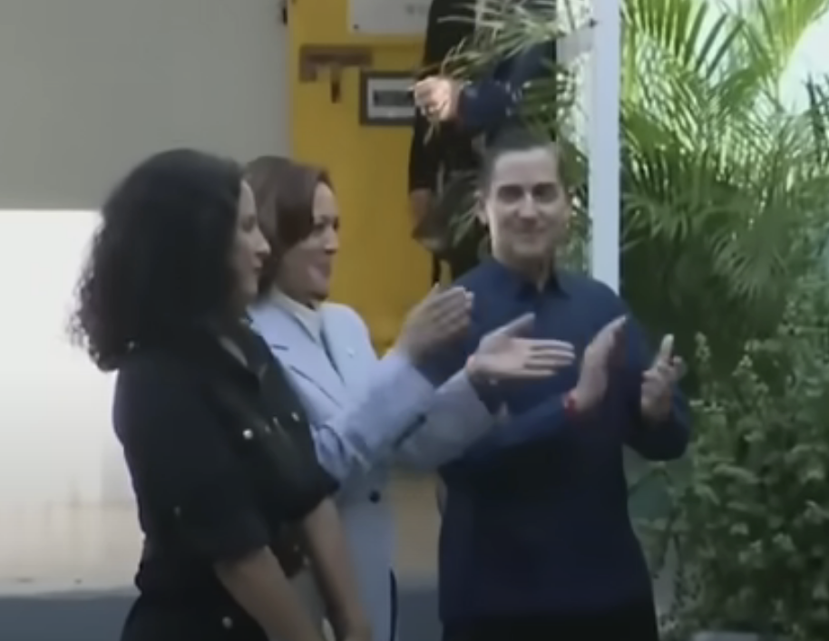 Kamala and two other people conversing outside a building, with Kamala and one of the other people clapping