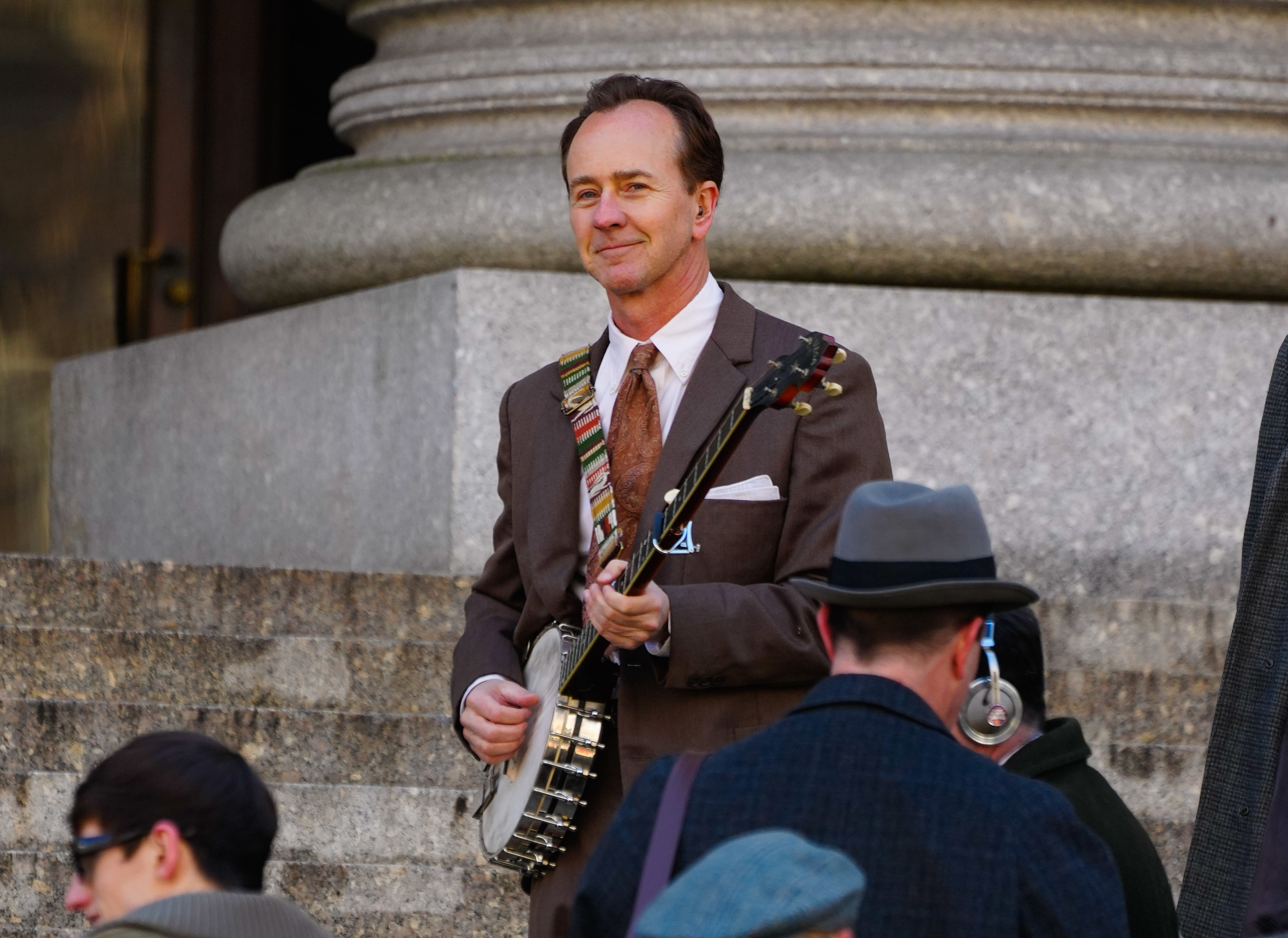 Edward in a suit holding a banjo with other people nearby