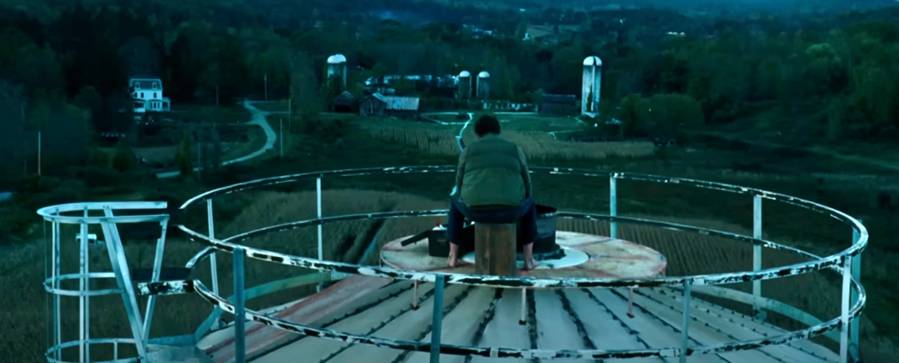 Lee Abbott sitting alone on top of a large circular structure in a rural setting at dusk
