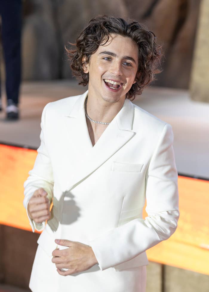 Timmy in a white suit and necklace at an event, smiling