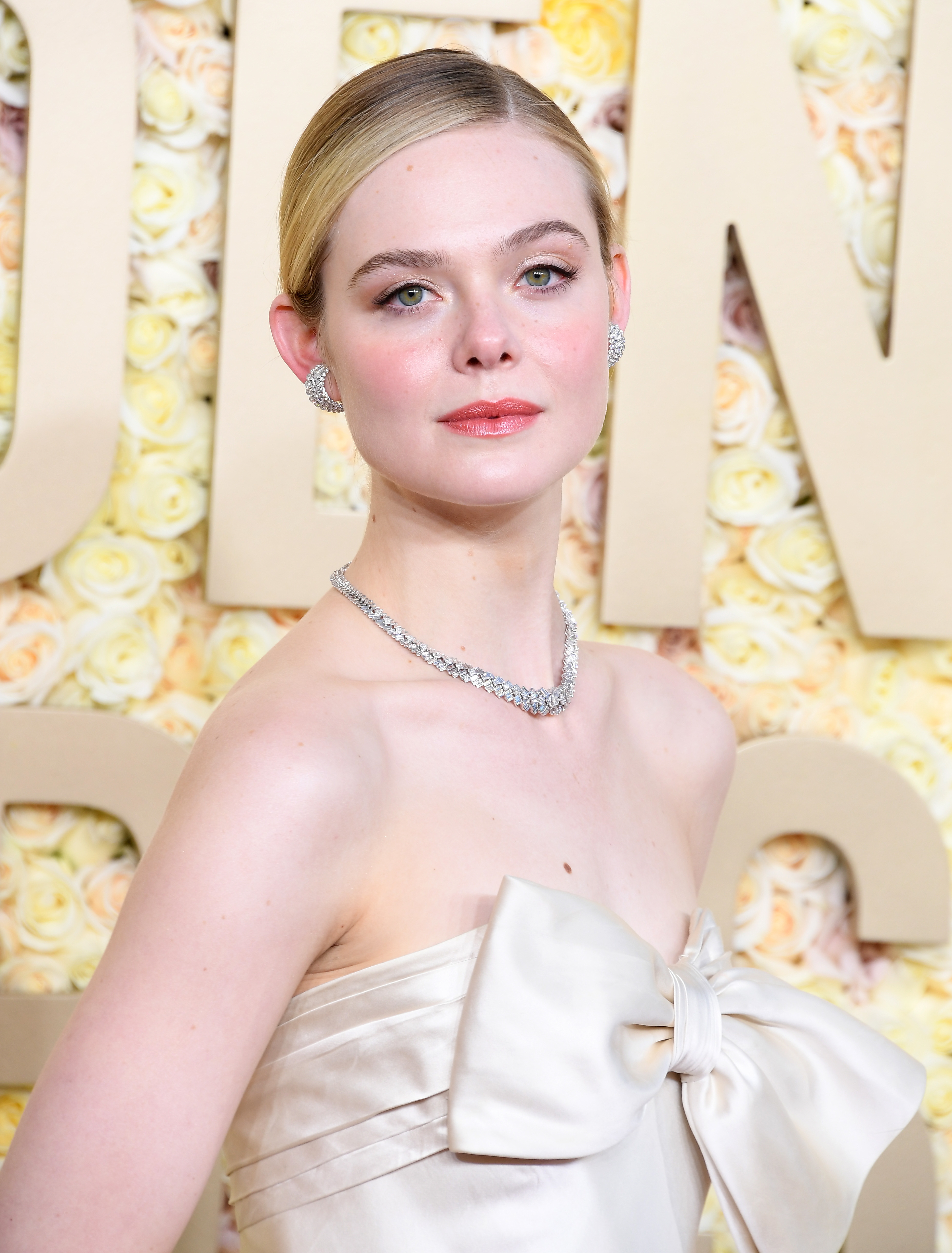 Elle Fanning in an off-shoulder gown with a bow detail, diamond necklace, and earrings at an event
