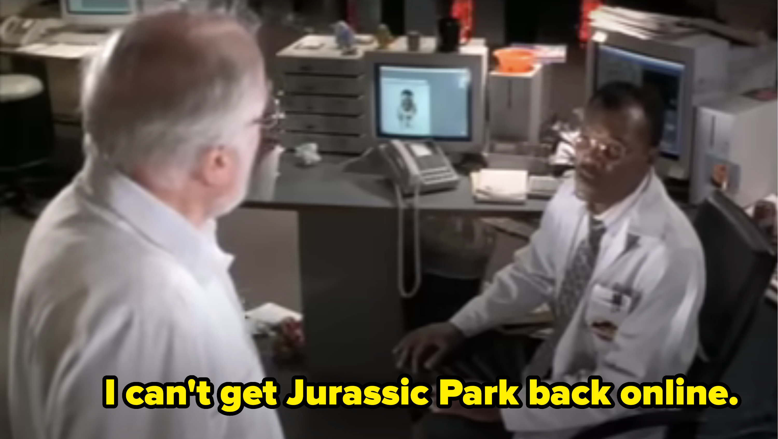 Two men in a laboratory setting, one seated at a desk with a computer showing a face, the other standing; Samuel L Jackson&#x27;s character says he can&#x27;t get Jurassic Park back online