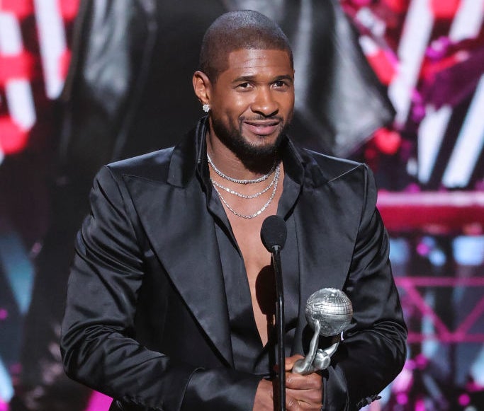 Usher in a black suit and shirt, holding an award onstage, smiling