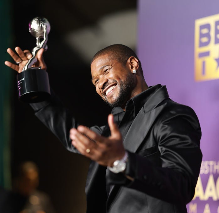 Usher in a suit holding up an award onstage and smiling