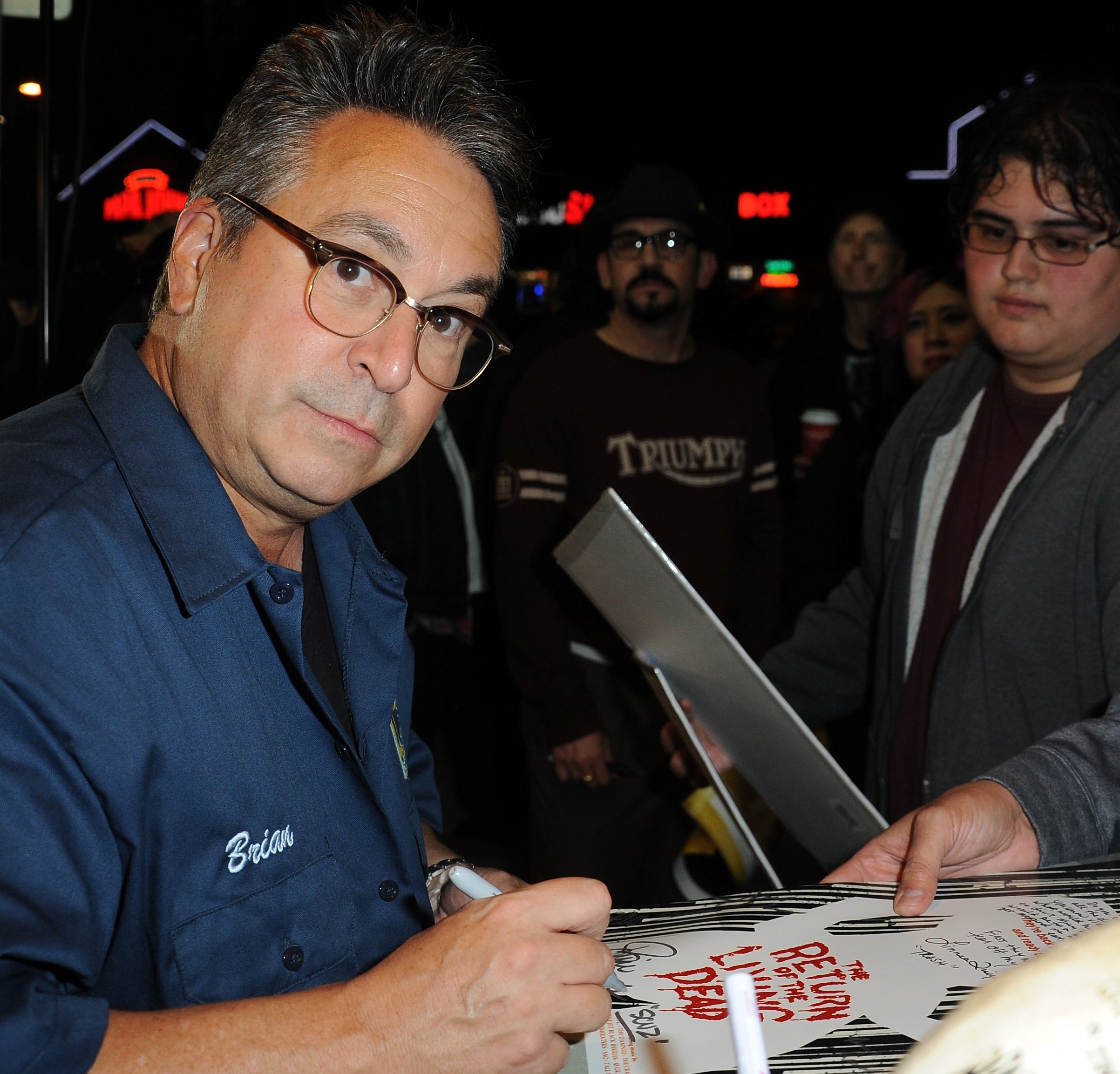 Brian Peck in glasses and blue shirt signing autographs for fans
