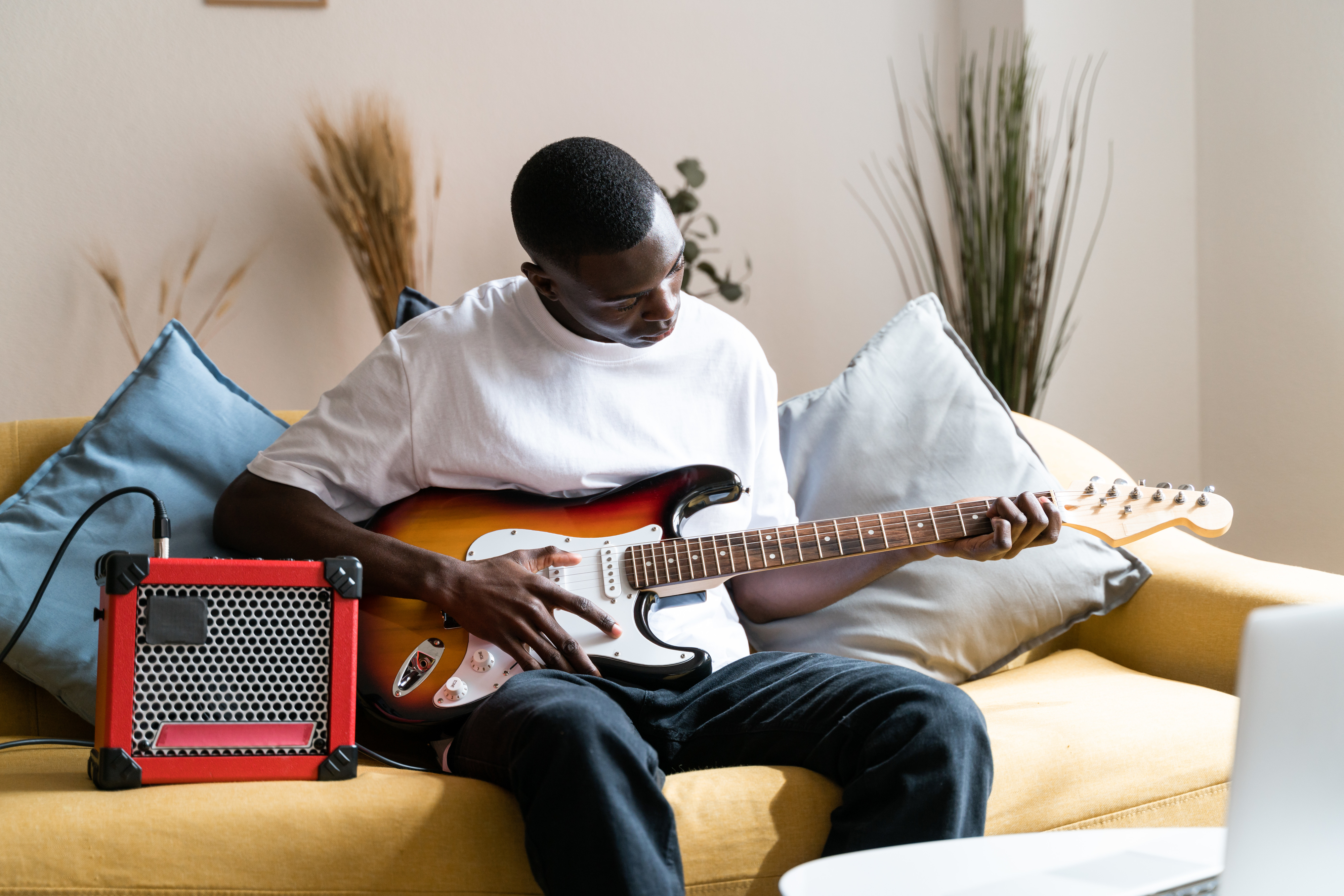 Person playing electric guitar seated on couch with small amplifier nearby