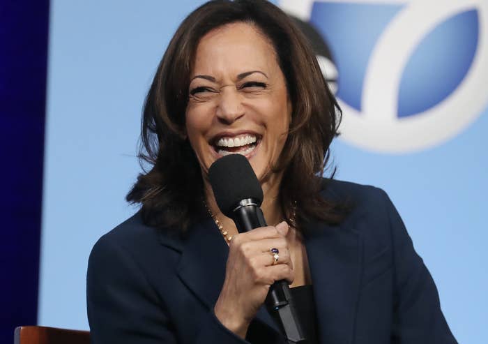 Kamala laughing and holding a microphone, wearing a suit jacket