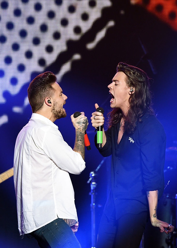 Two singers, one with tattoos, performing on stage with microphones