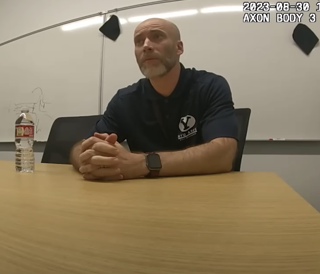 Kevin seated in a room with a table, water bottle, and wearing casual attire