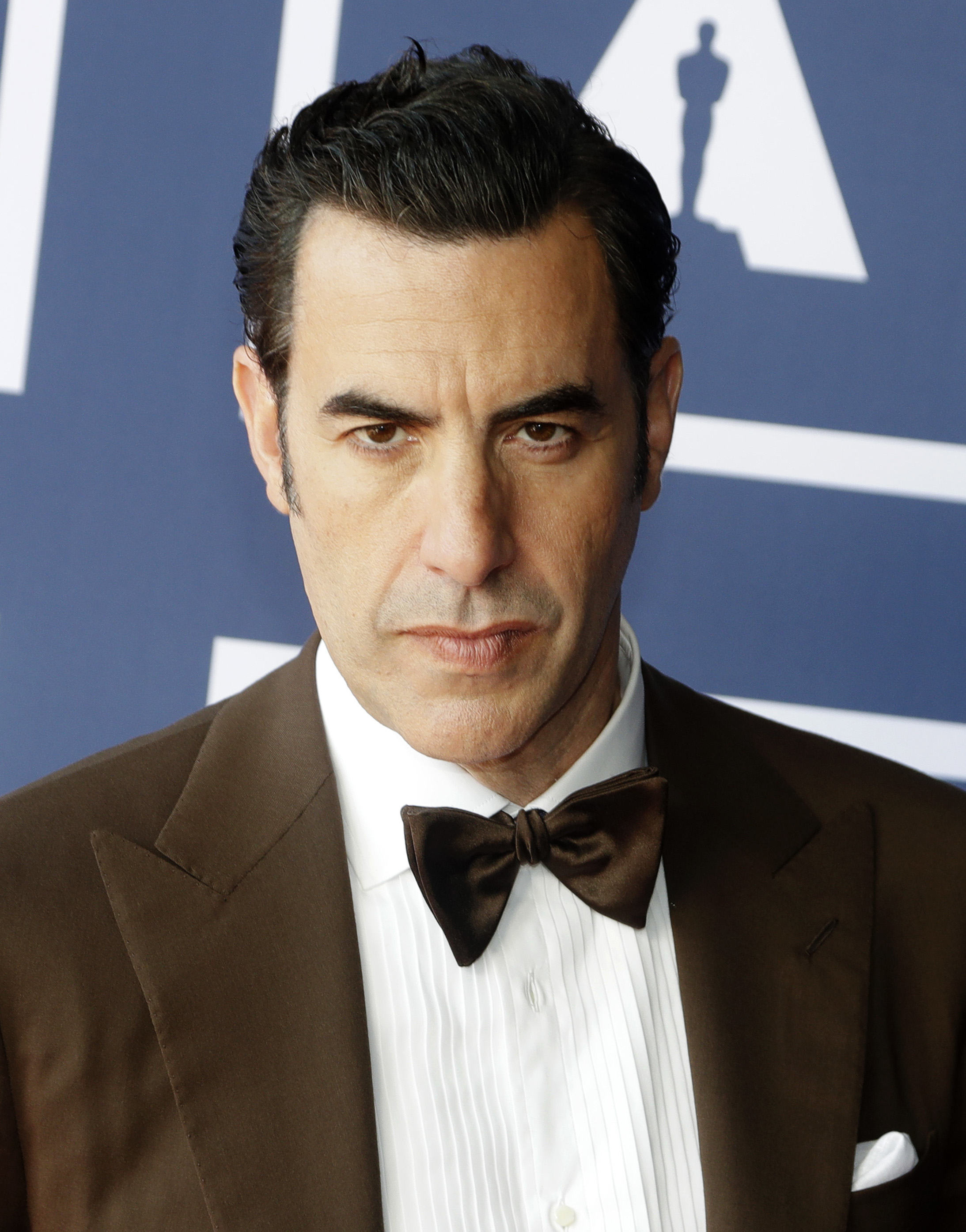 Sacha Baron Cohen in a brown suit and bow tie at an event