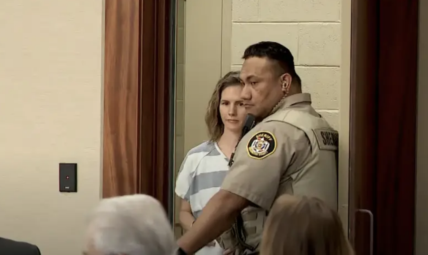 Ruby in a striped uniform stands next to a law enforcement officer in a courtroom