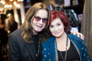 Two individuals standing close together, one with a long hairstyle and glasses, the other with a short red hairstyle, both in stylish attire