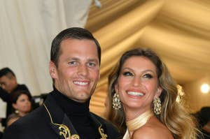 Tom Brady and Gisele Bündchen smiling at an event, Brady in a black outfit with gold detailing, Bündchen in an off-the-shoulder gold gown