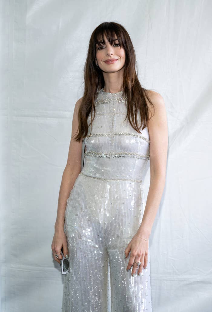 Anne Hathaway in a sleeveless sequin jumpsuit, standing against a plain backdrop