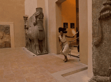 Mujer corriendo en un pasillo de museo con esculturas antiguas