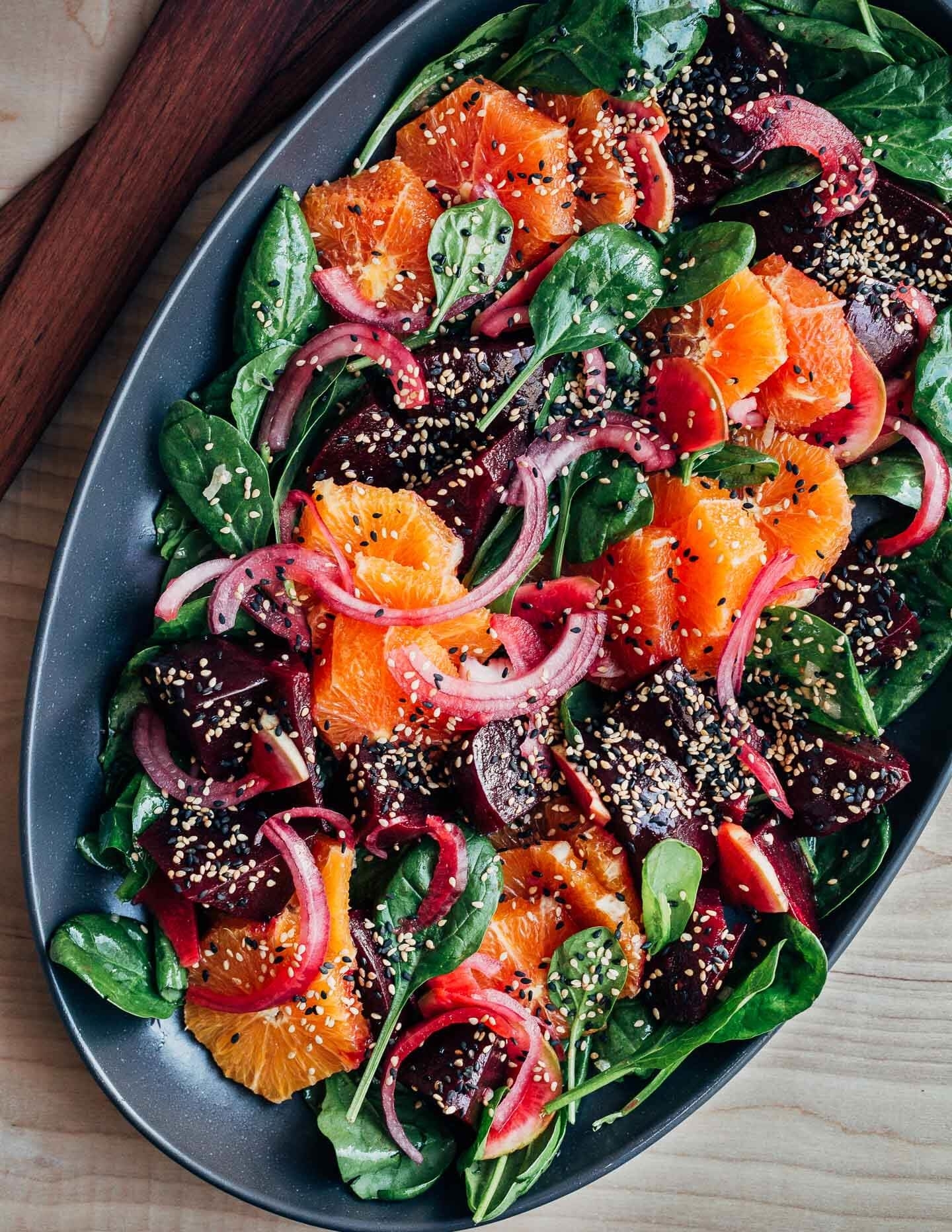 Salad with spinach, sliced oranges, beets, pickled onions, and sesame seeds served in a black oval dish