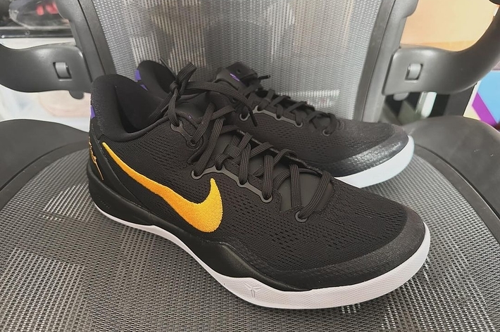 A pair of black sneakers with a distinctive golden swoosh on a textured surface