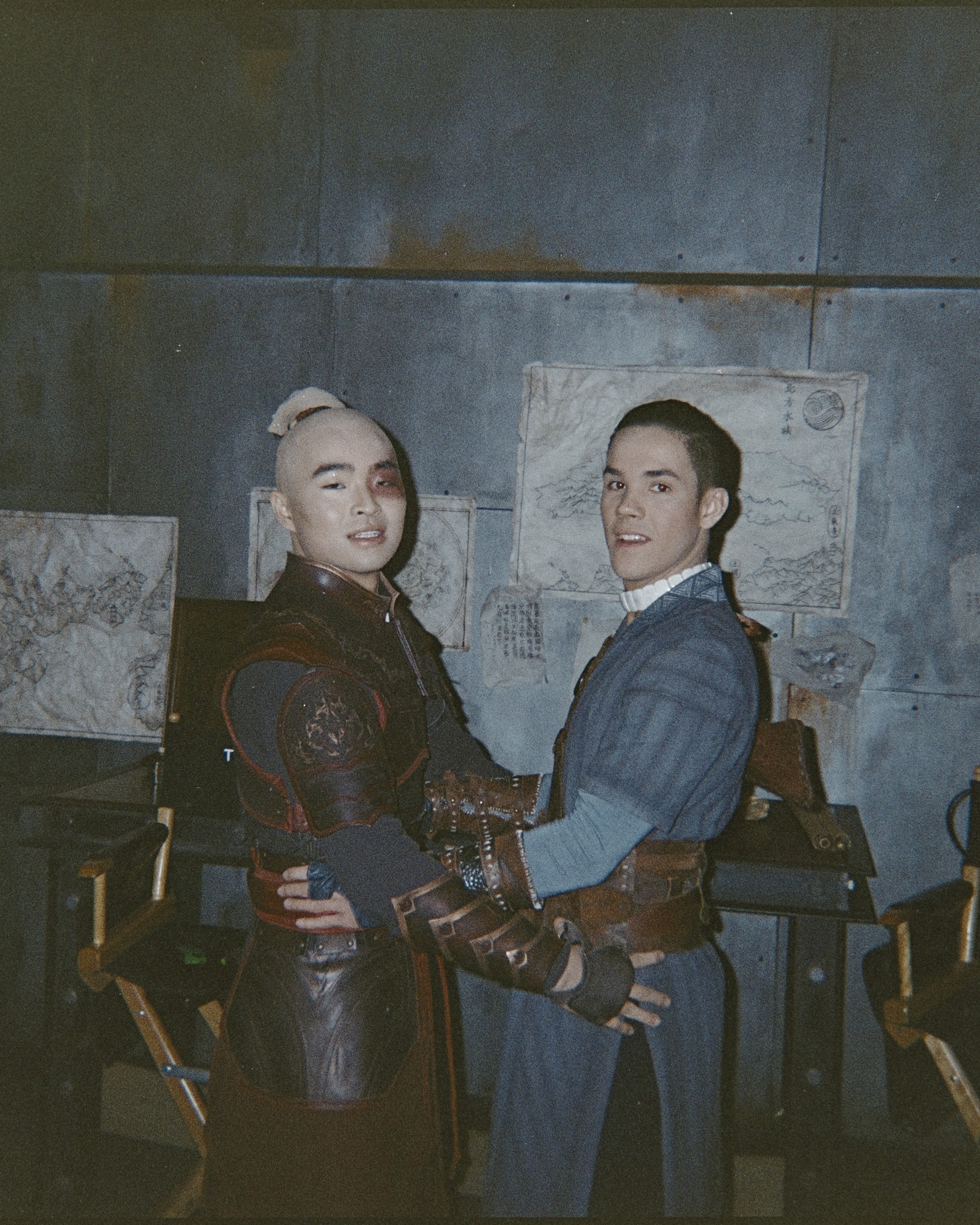Two actors on set, one in armor and one in a suit, smiling at the camera