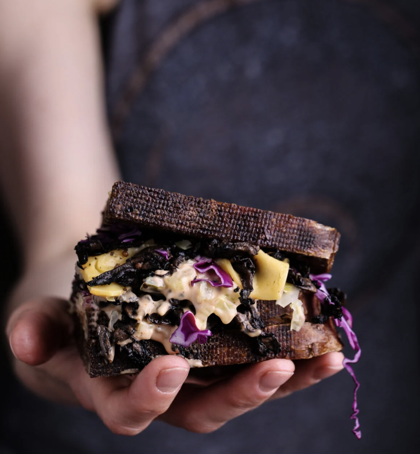 Person holding a sandwich with dark bread, filled with cheese and cabbage