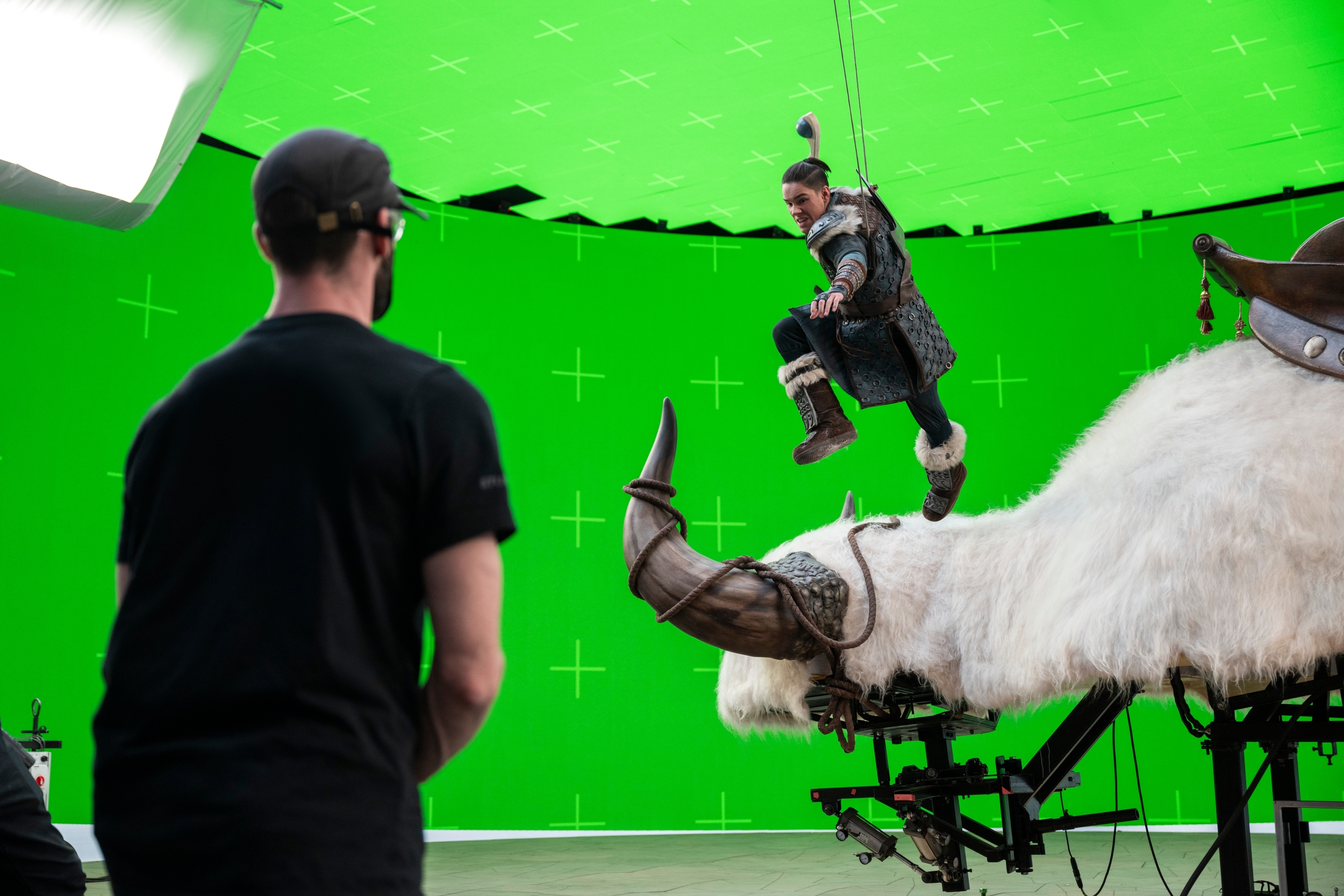 Actor in costume performs on mechanical bull against green screen with technician watching