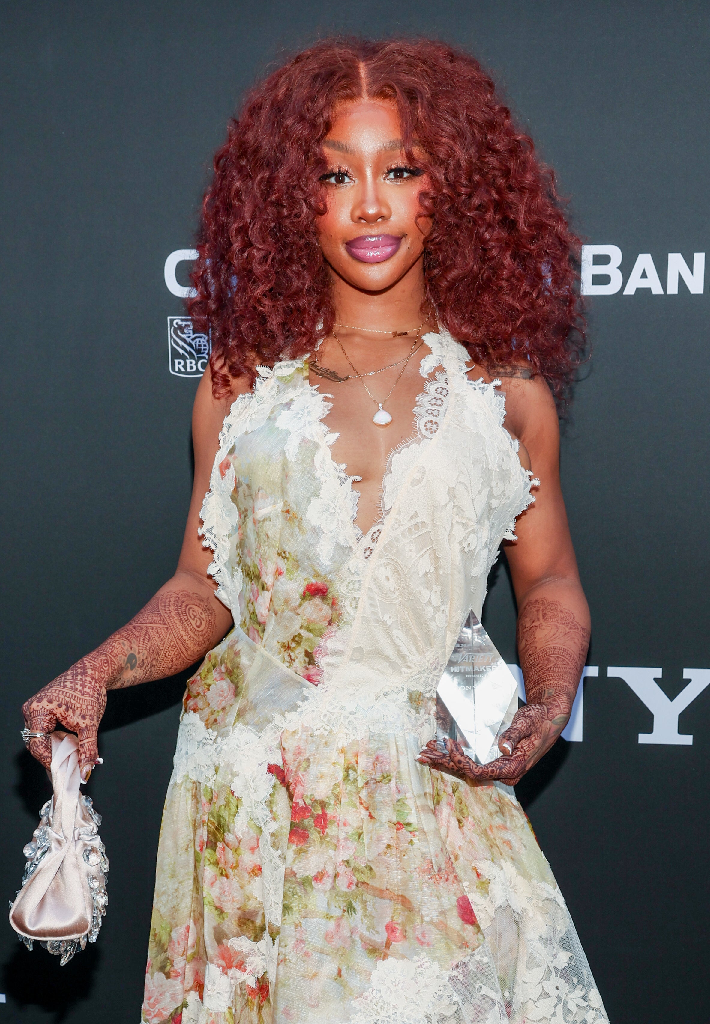 SZA in floral, lace dress and pink shoes poses on event backdrop