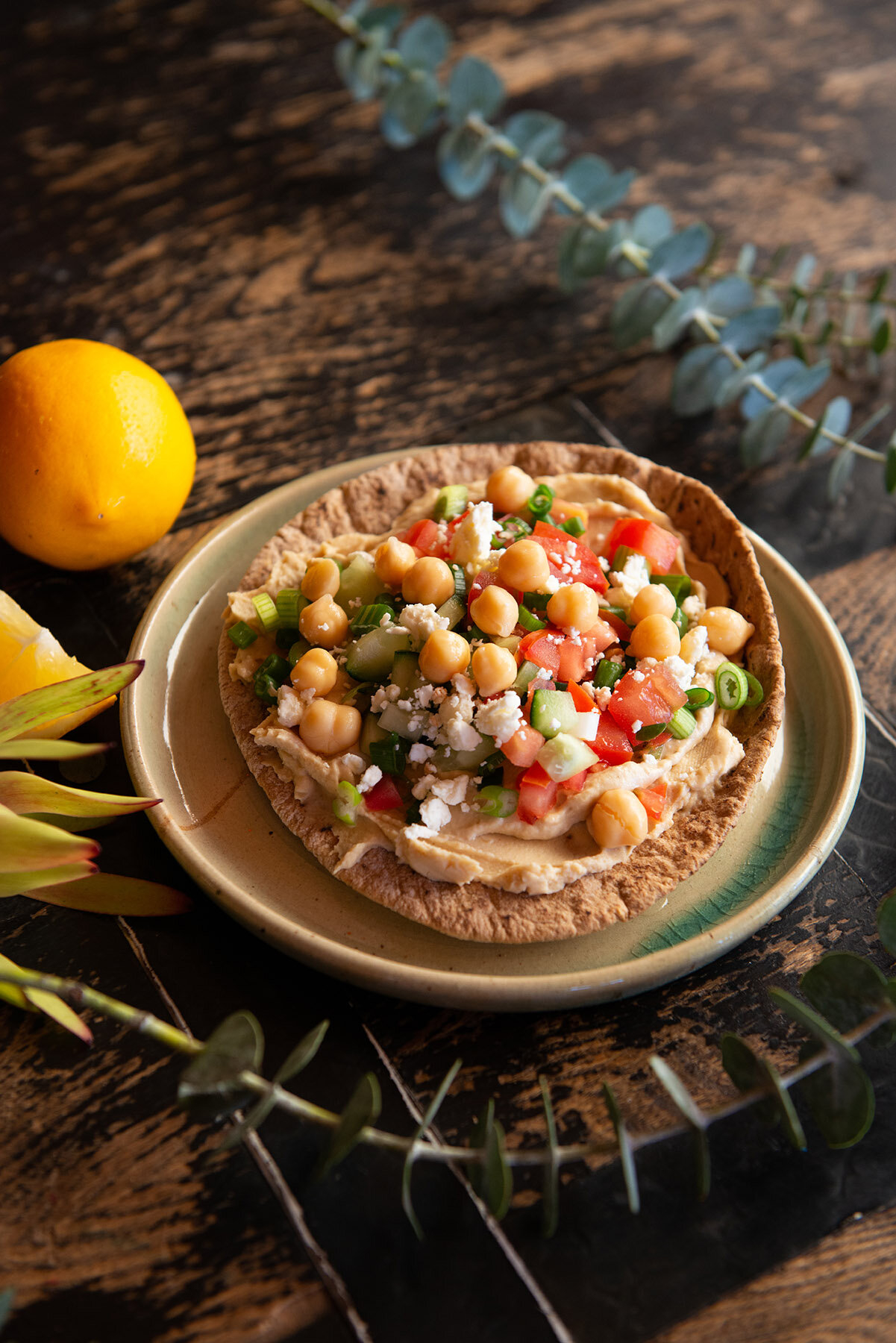 Plate with hummus topped with chickpeas, tomatoes, and herbs, next to a lemon