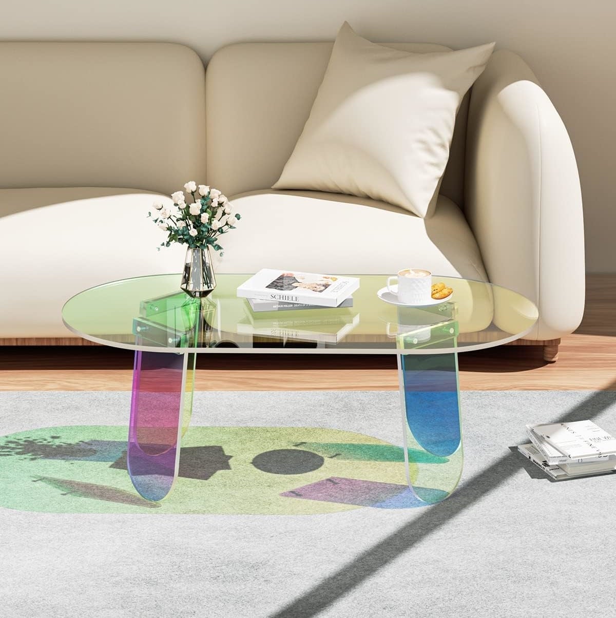 Transparent coffee table with books in a living room, featuring a rug and a beige sofa