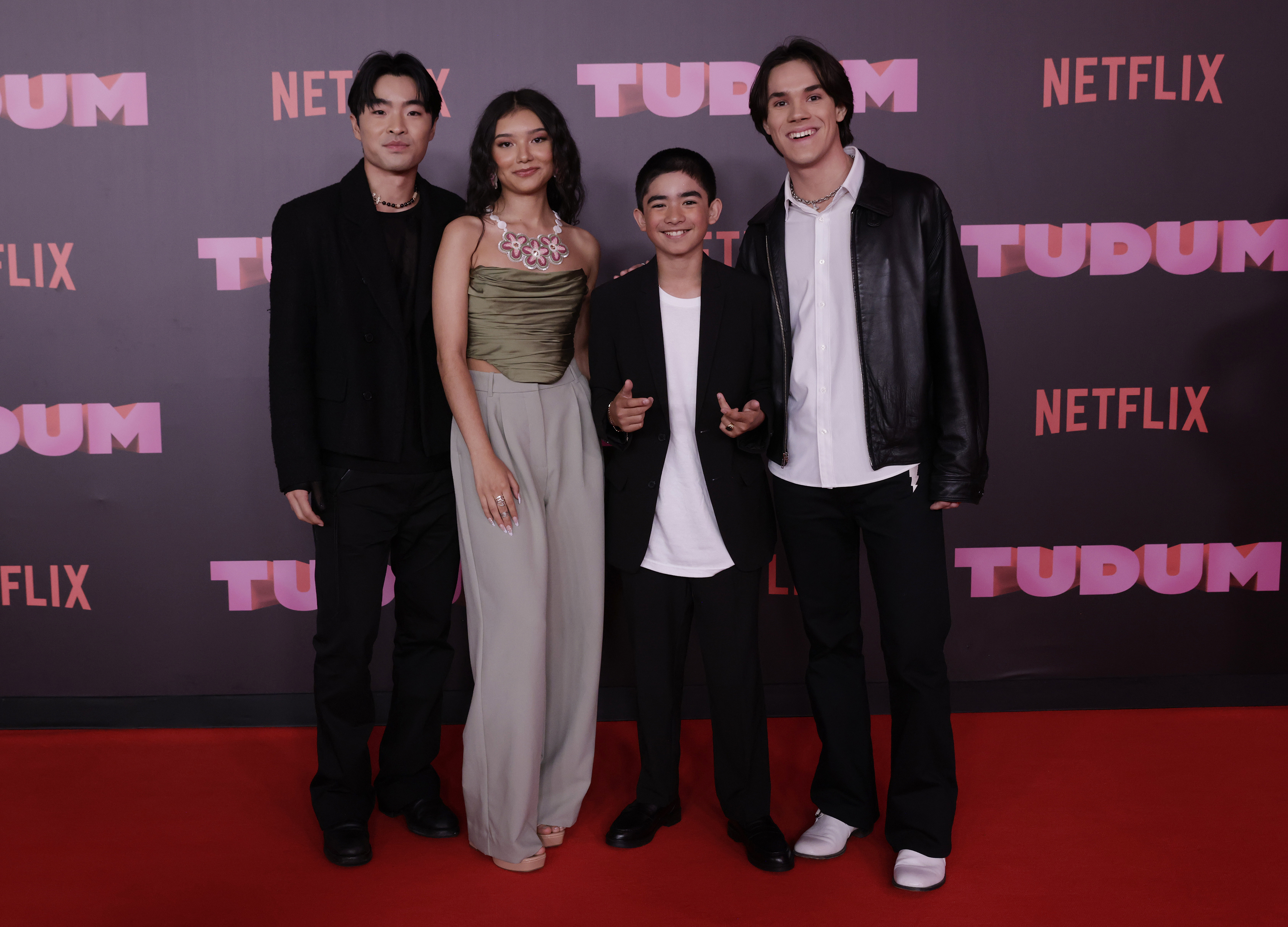 Four cast members posing at a Netflix event, two in suits, one in a dress, one in casual wear