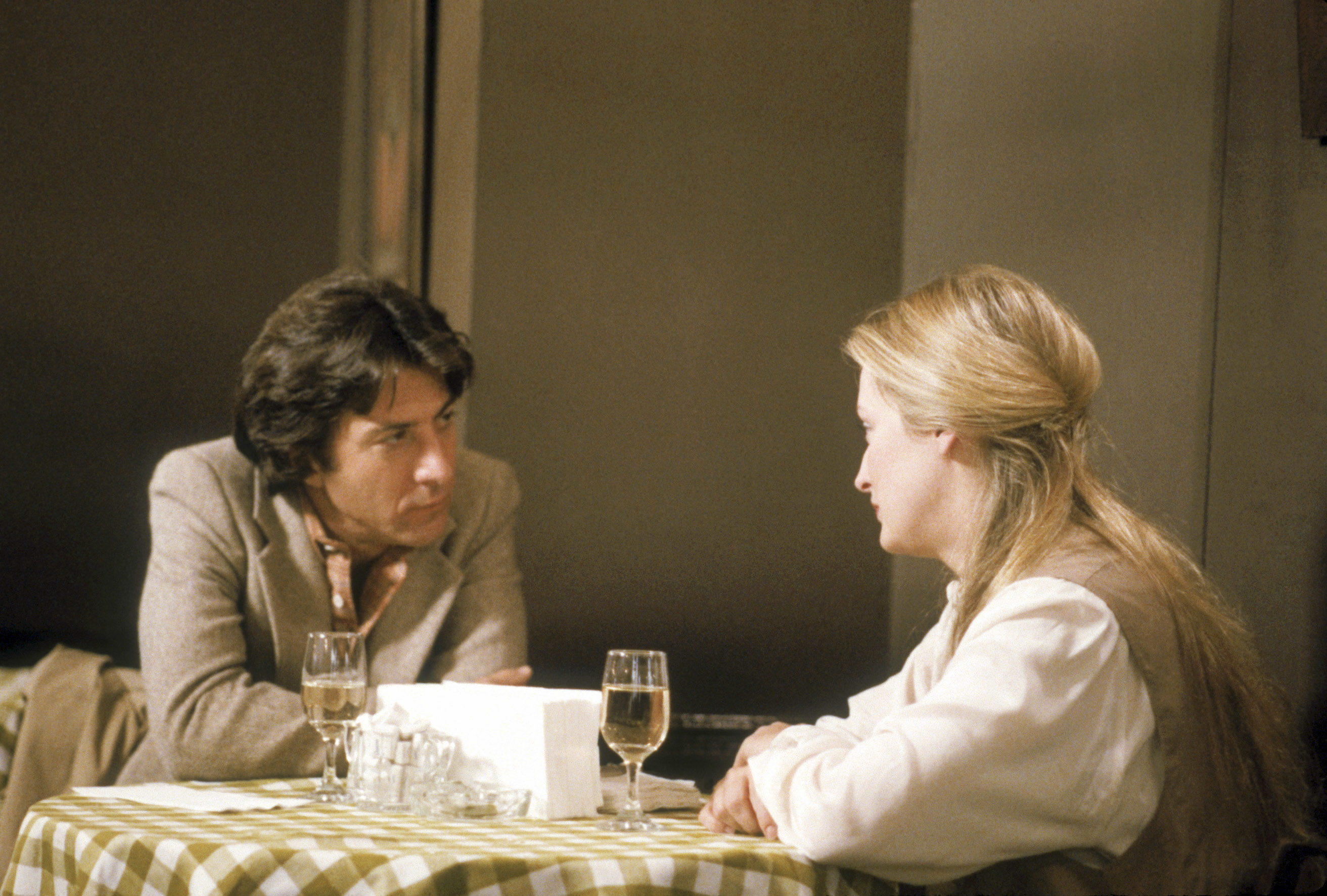 In a scene, Dustin appears attentive while Meryl speaks, set in a dining setting with a checkered tablecloth