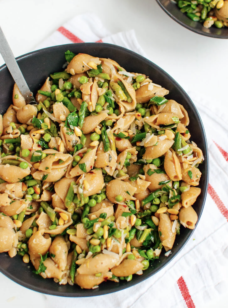 A bowl of pasta with peas and greens, garnished with pine nuts
