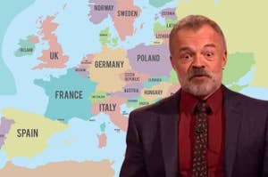Graham Norton in a buttoned shirt and jacket stands before a map of Europe
