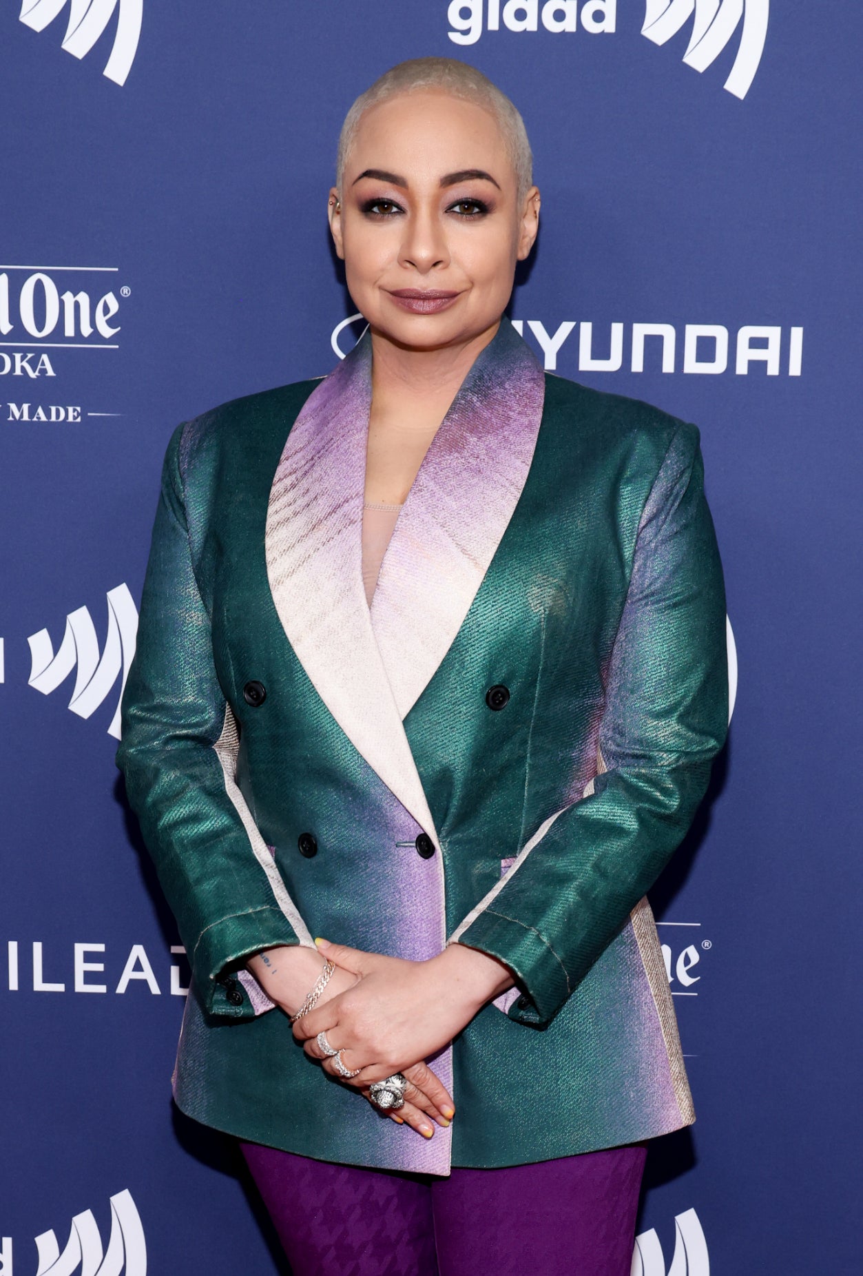Raven-Symoné posing at an event in a green blazer, purple pants, and matching shoes