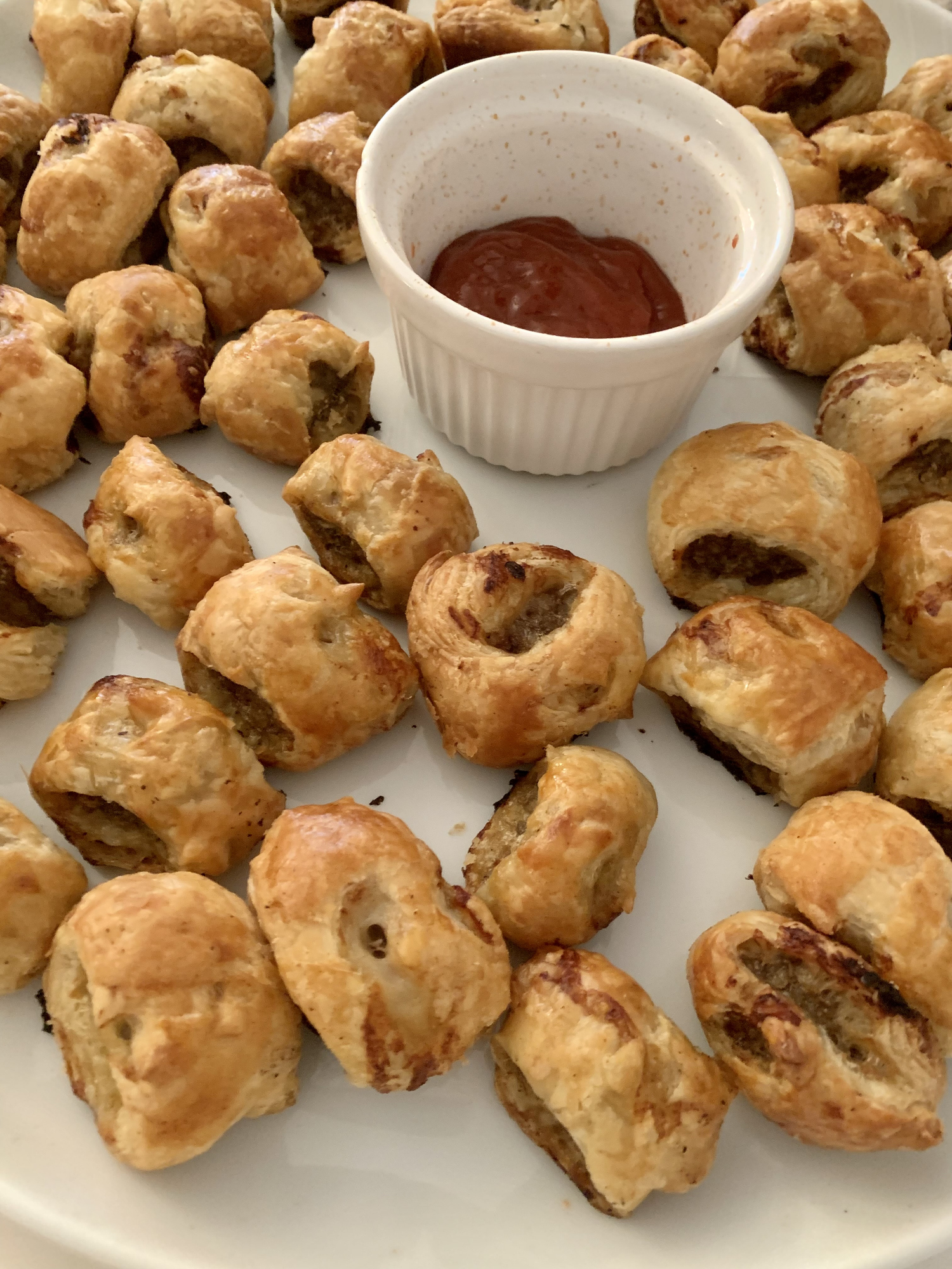 A platter of sausage rolls with a bowl of dipping sauce in the center