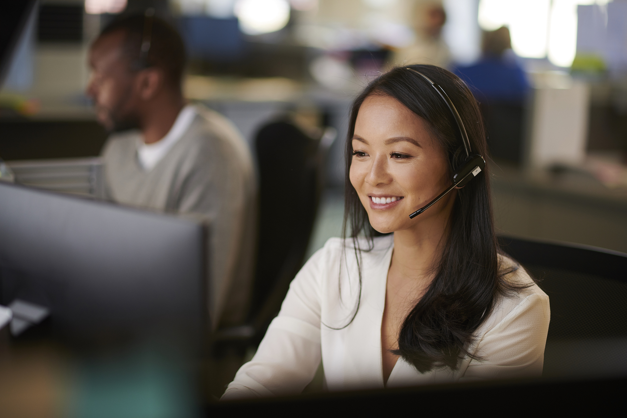 Woman in headset smiling at desk, representing customer service in a modern workplace setting