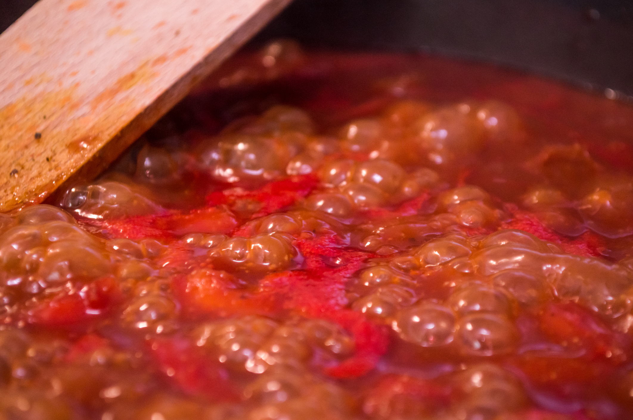Close-up of a wooden spoon stirring bubbling tomato sauce in a pan