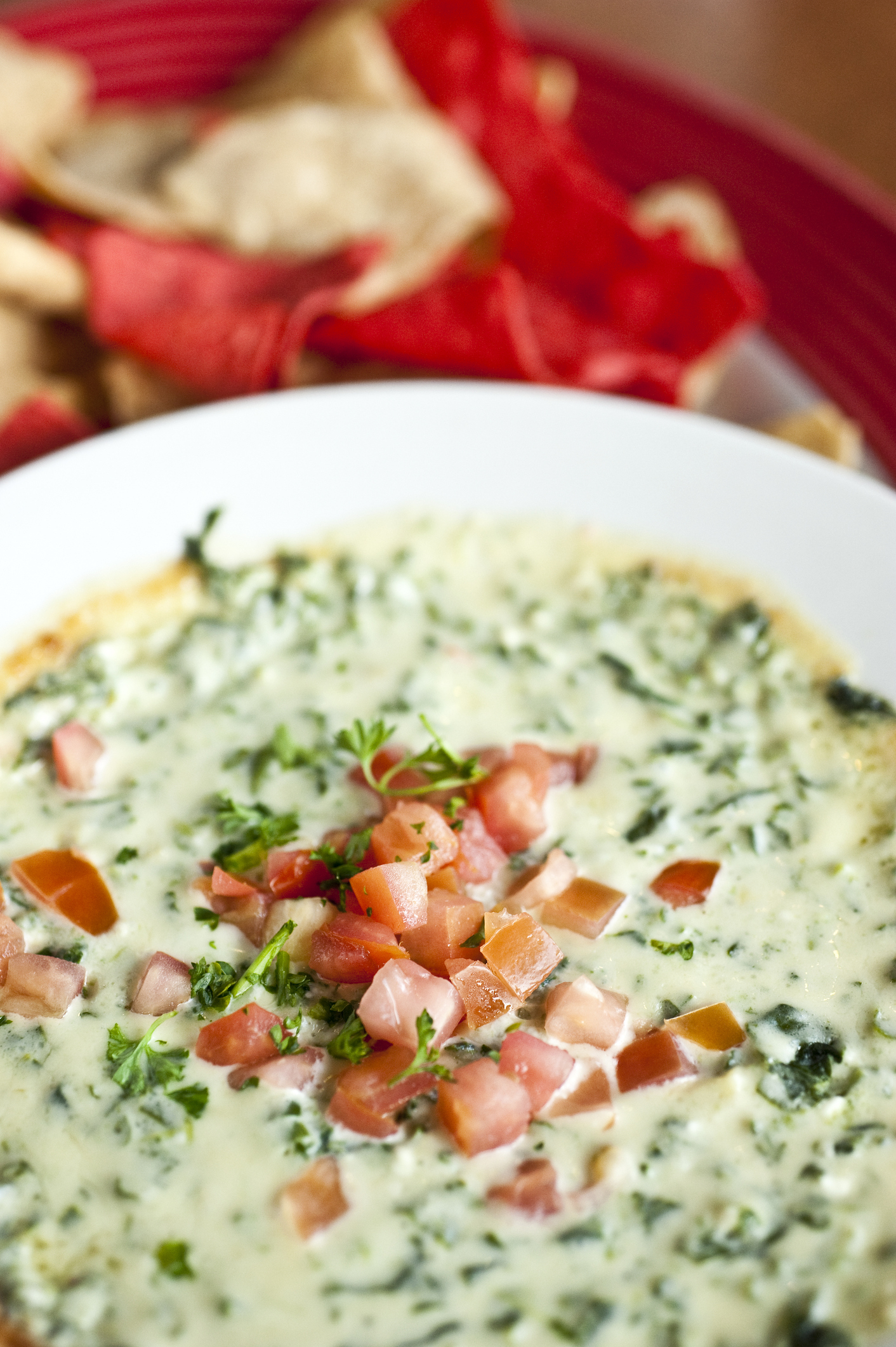 Spinach dip in a white bowl topped with diced tomatoes, served with tortilla chips