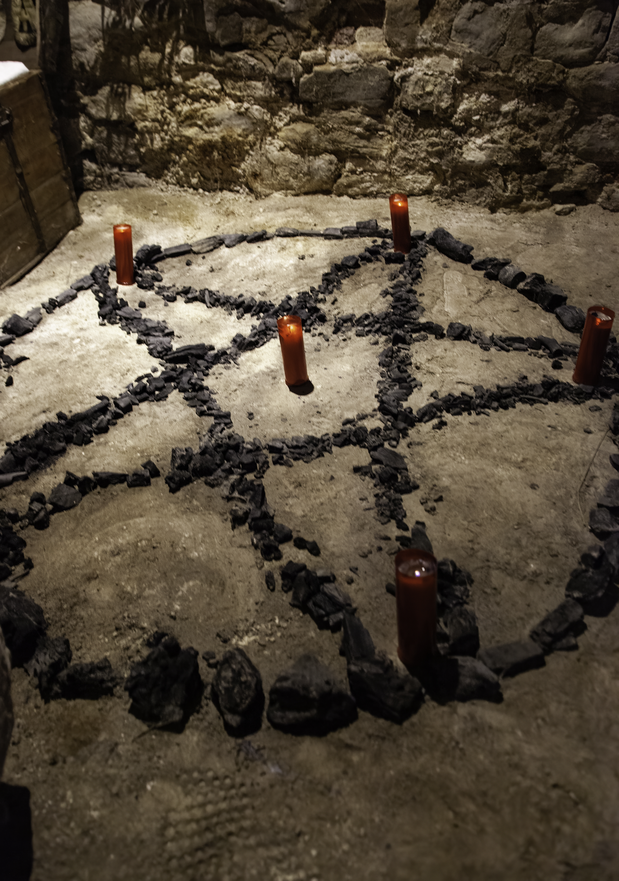 Pentagram shape made of stones on the ground with candles at each point in a dimly lit setting