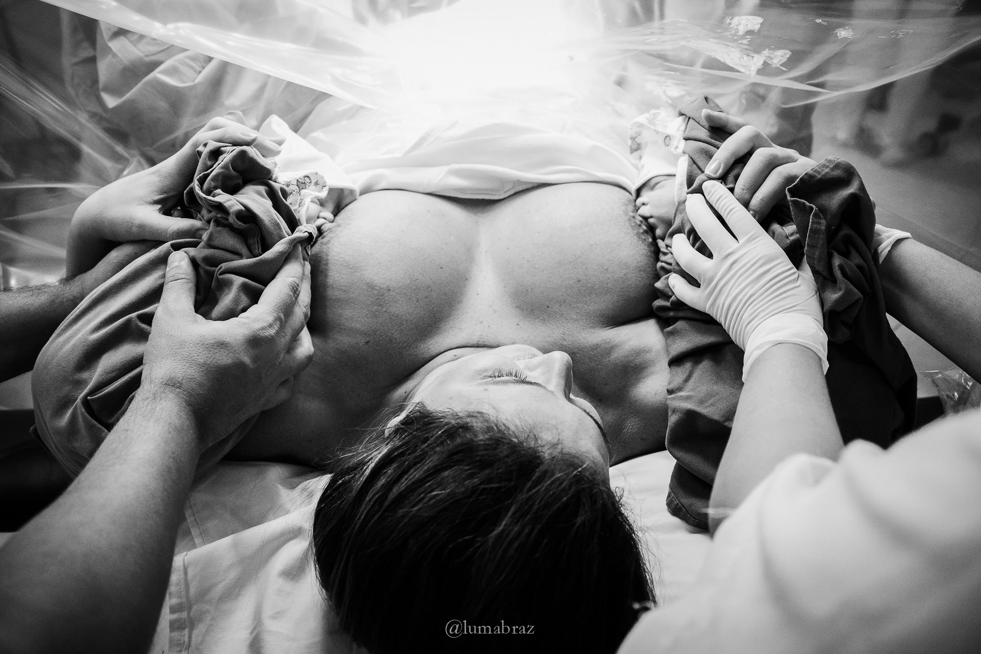 A mother holds her newborn against her chest in a hospital setting after delivery