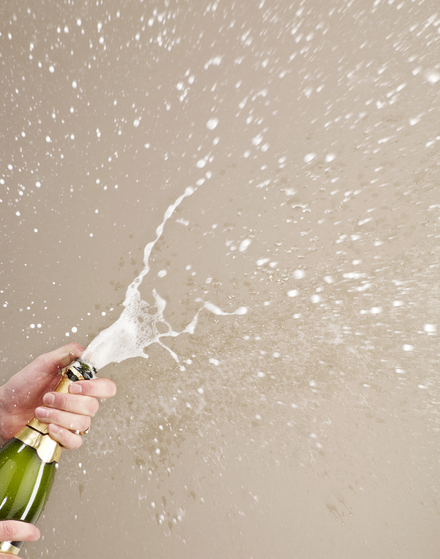 Hand holding a champagne bottle with cork popped and foam spraying out,