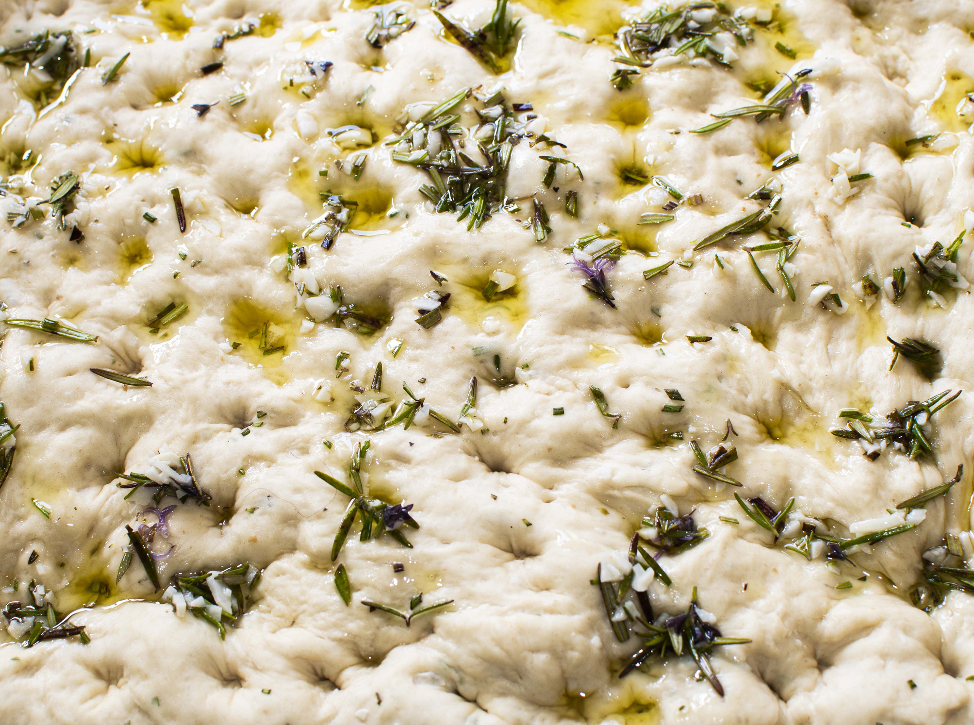 Close-up of freshly prepared focaccia bread dough topped with herbs and oil before baking