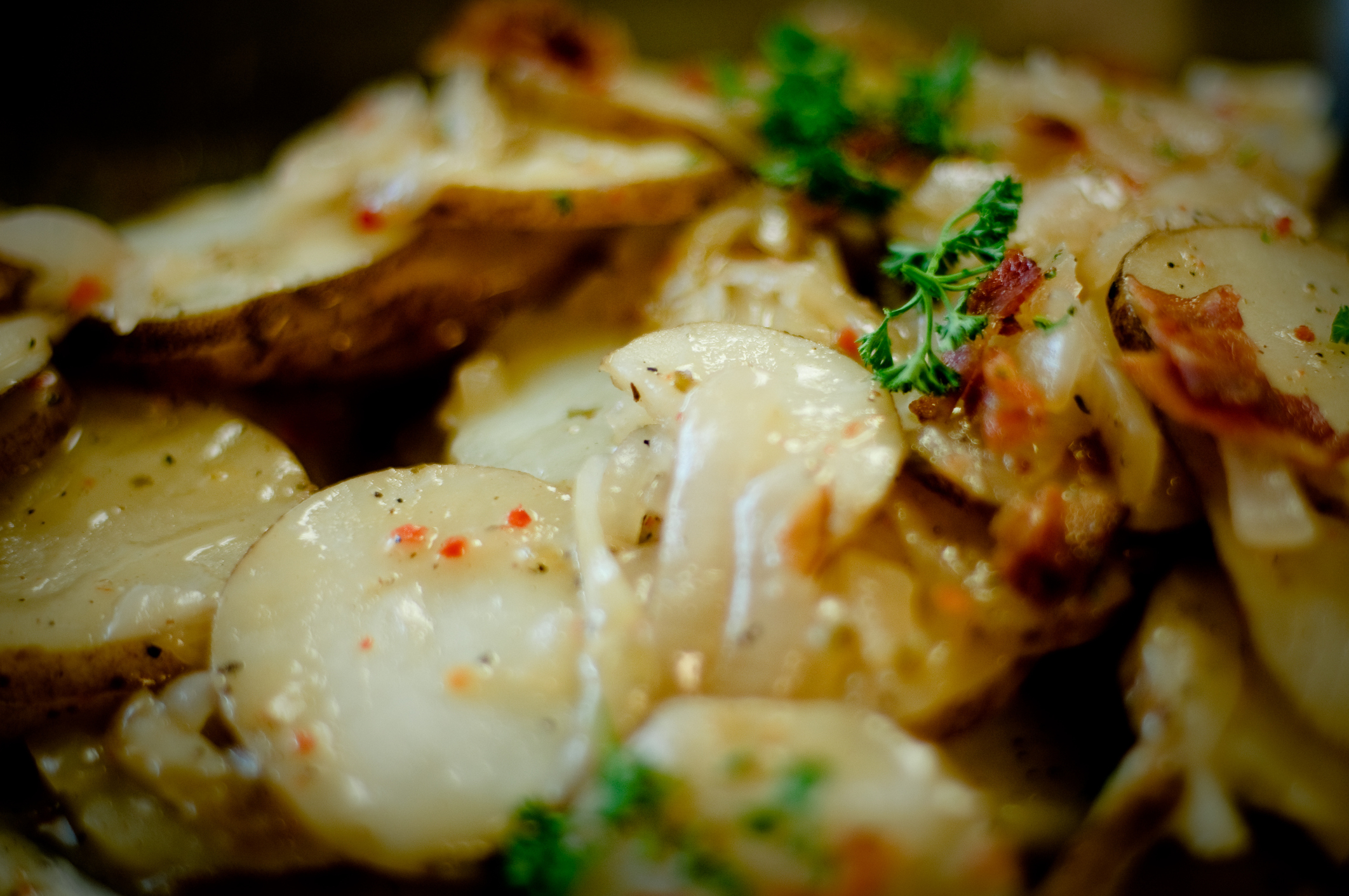 Close-up of a dish with sliced potatoes, herbs, and bacon