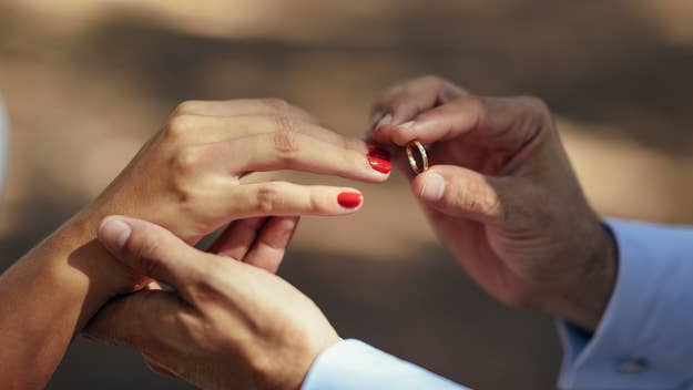 Two hands exchanging wedding rings, one with red nail polish