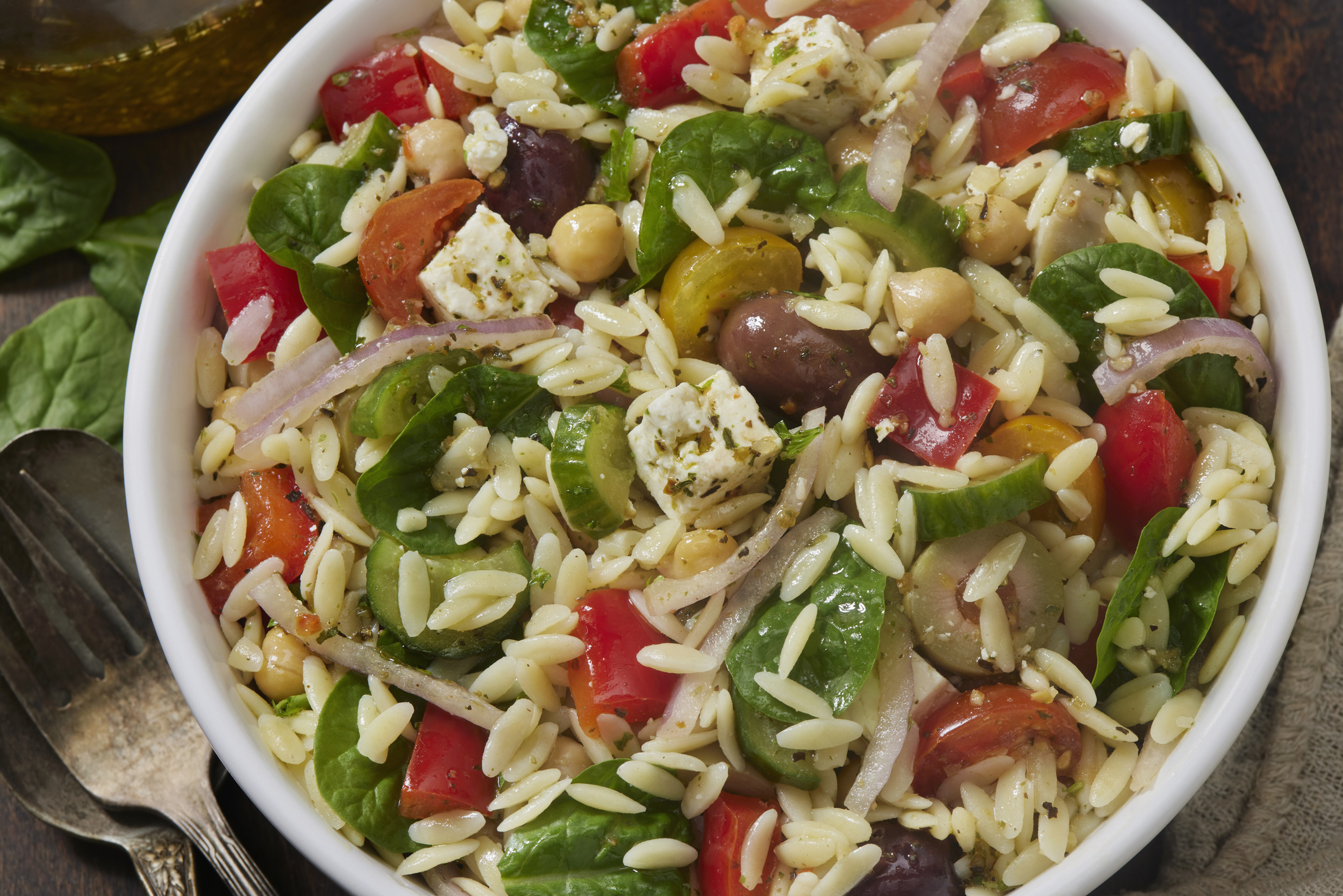 A bowl of orzo pasta salad with spinach, tomatoes, onions, chickpeas, olives, and feta cheese
