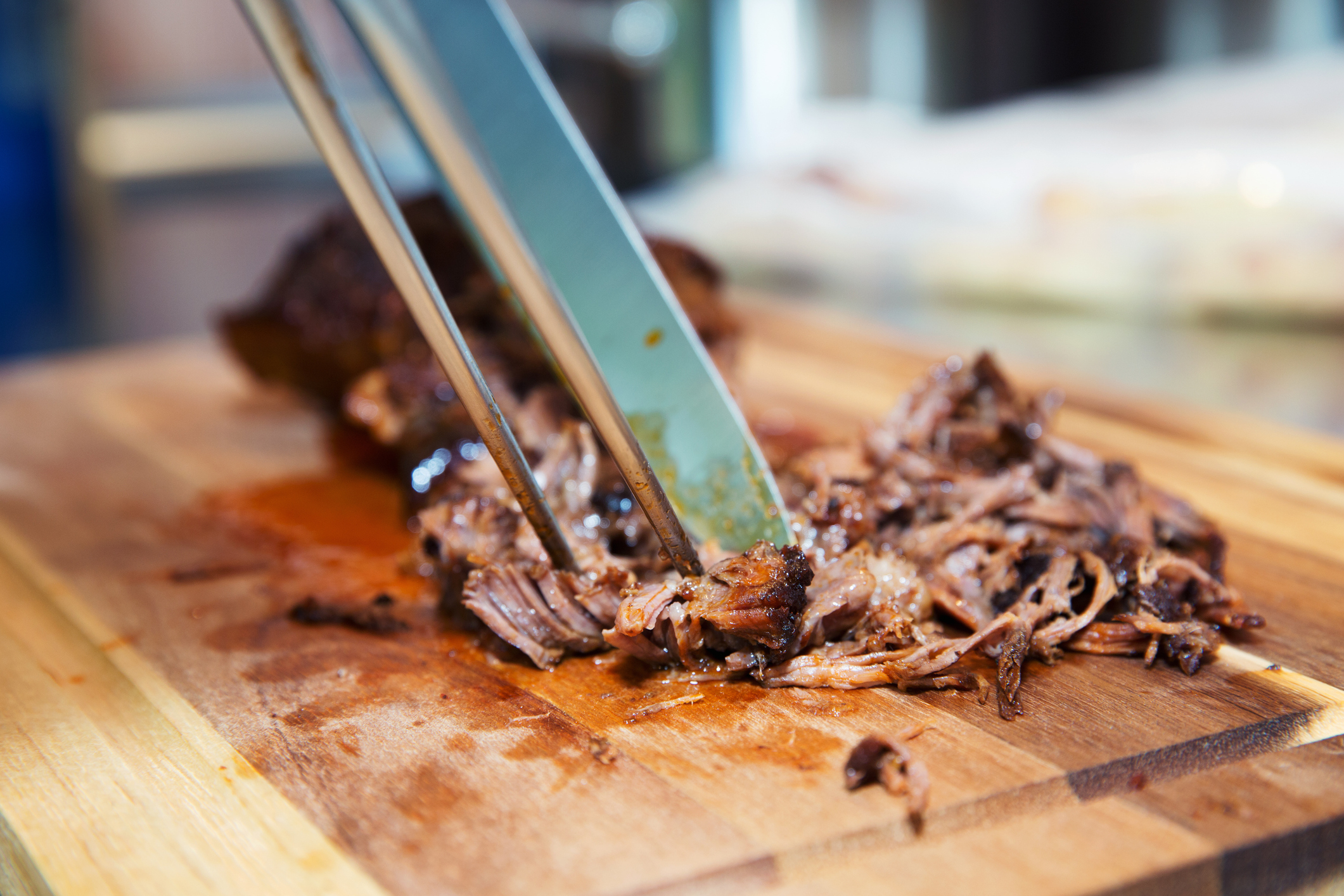 Shredded meat on a cutting board with tongs pulling it apart