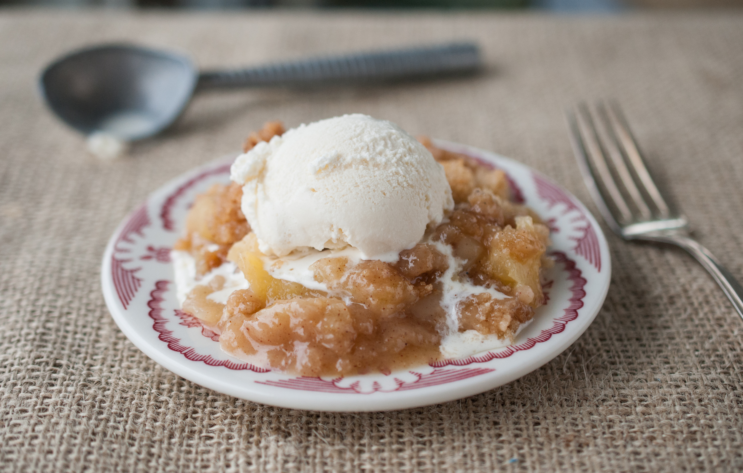 A plate of apple cobbler topped with a scoop of vanilla ice cream, with a spoon on the side