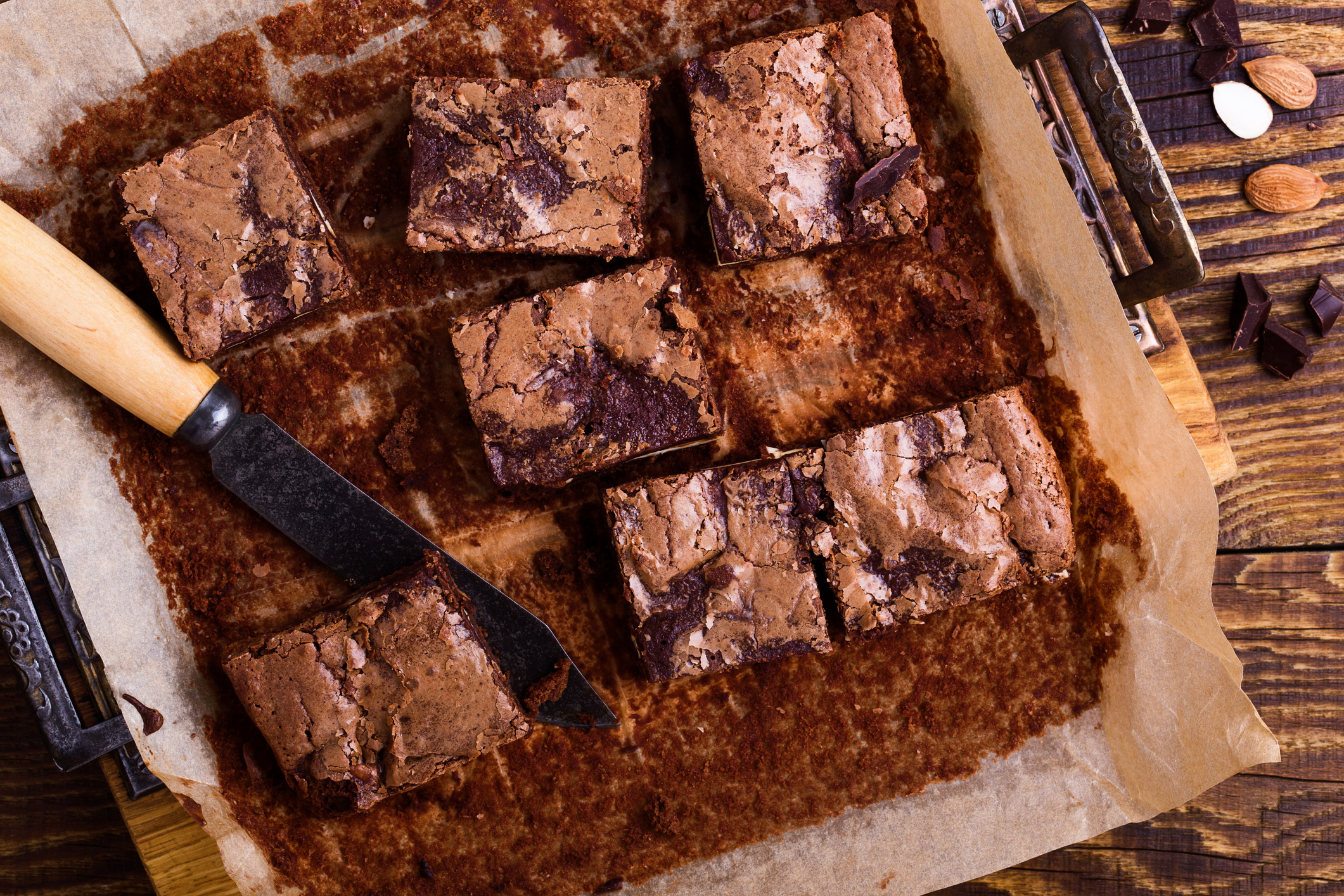 Freshly baked brownies in a pan with a knife, surrounded by scattered nuts and chocolate pieces