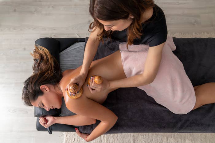 A person receiving a back massage with wooden tools from a massage therapist