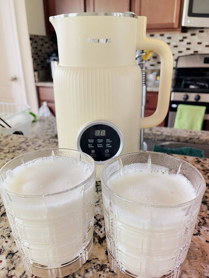 nut milk maker with two glass mugs filled with frothed milk on a kitchen counter