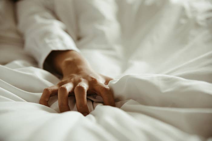 Close-up of a person&#x27;s hand gripping bedsheets, suggesting intimacy