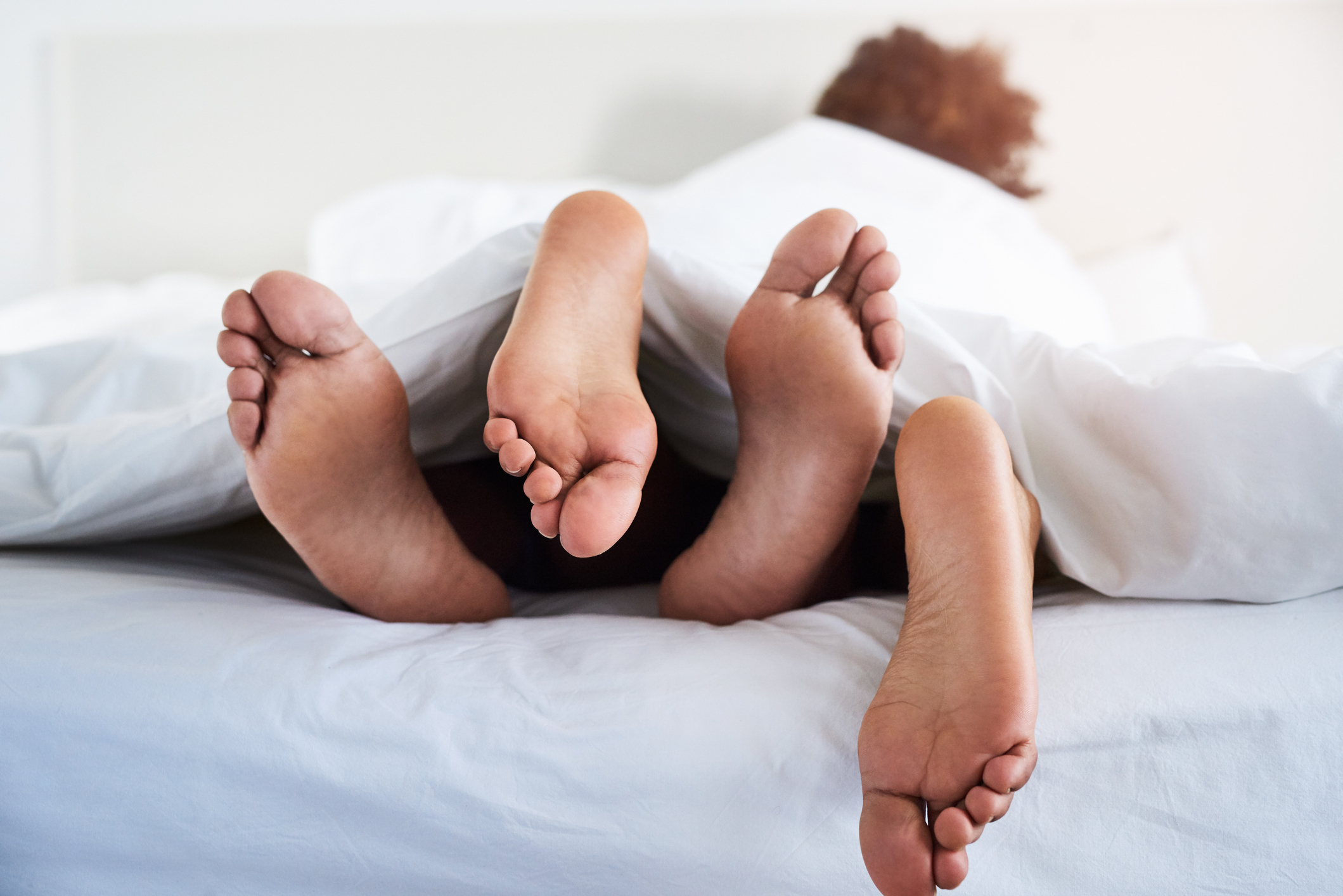 Two pairs of feet stick out from under bed sheets, suggesting an intimate moment
